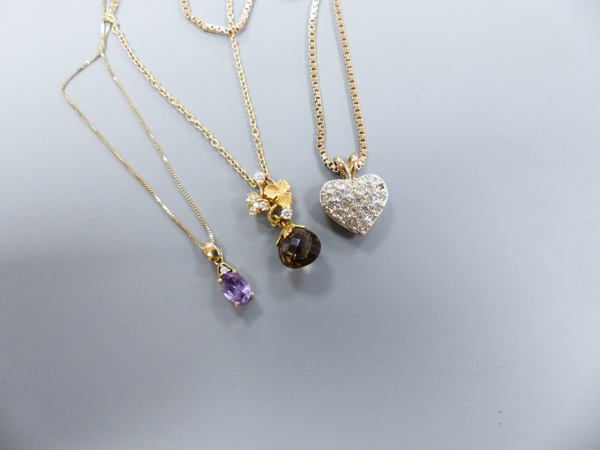 A smoky quartz pear-shaped pendant on diamond-set 'leaf' suspension and 9ct gold chain, a 9ct gold box-link chain with paste 'heart' pendant and a 9ct gold and amethyst pendant on 9ct gold fine chain.